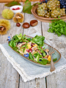 Chestnut salad with grapes, orange, lamb's lettuce and pomegranate in an elongated bowl on a cloth, untreated wooden table with chestnuts, peels and chervil Chestnut salad with grapes, orange, lamb's lettuce and pomegranate in an elongated bowl on a cloth, untreated wooden table with chestnuts, peels and chervil